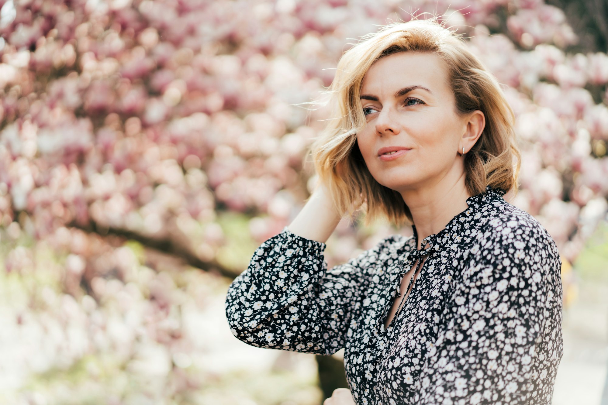 Beautiful woman in her forties. Profile portrait with a pink flowering magnolia tree as background.