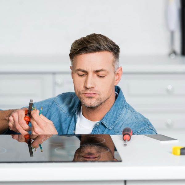 handsome man repairing electric stove at kitchen